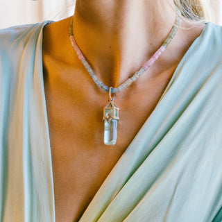 Necklace with a clear crystal pendant worn by a person draped in light fabric.