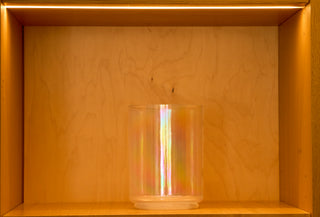 Iridescent apophyllite and platinum singing bowl in warm gold light, atelier shelf display, front view.