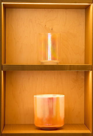 Iridescent apophyllite and platinum singing bowls displayed on gold-lit atelier shelving.
