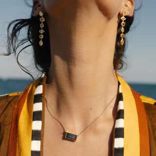 Gold necklace with bi-color tourmaline and diamond pendant, colorful outdoor lifestyle shot.