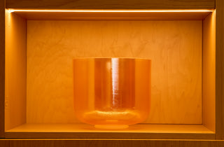 Citrine white light aura singing bowl glowing warm amber on lit atelier shelf, front view.
