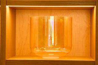 Large 13-inch crone goddess supergrade singing bowl glowing amber gold on lit wood shelf.
