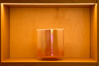 Iridescent Saint Germain sky singing bowl in warm gold light, atelier shelf display, front view.
