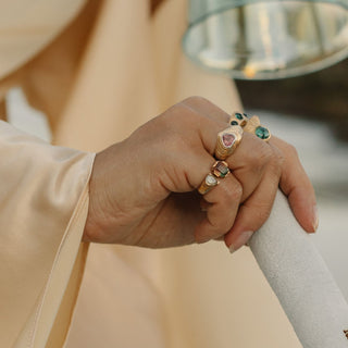 Gold pink tourmaline signet ring worn with layered rings, soft indoor lifestyle shot.
