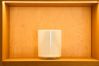 Larimar singing bowl in soft white displayed on warm wood atelier shelf, front view.
