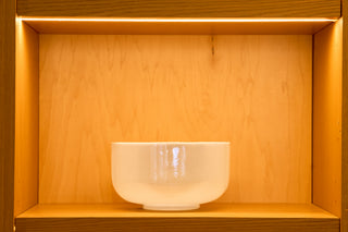 Large ocean indium alchemy singing bowl in creamy white on lit wood shelf, front view.
