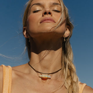 18k rose gold opal pendant worn outdoors in sunlight, eyes closed, lifestyle portrait.