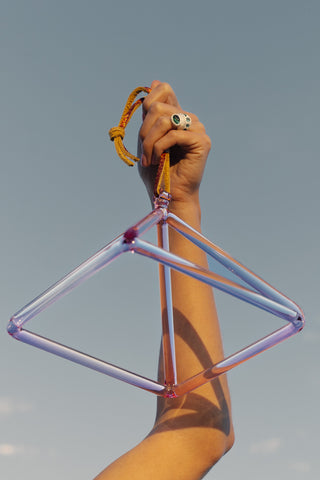 Pink aura gold crystal pyramid held overhead against blue sky, close hand detail.
