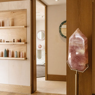 Sanamama showroom hallway with rose quartz tower on stand and crystal collection on wood shelving.
