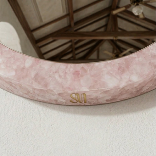 Close detail of rose quartz mosaic mirror frame with Sanamama logo in gold, wall-mounted.